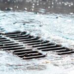 Rain falling and draining from a road into a stormwater drainage grate.