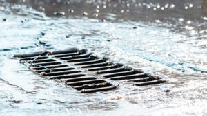 Rain falling and draining from a road into a stormwater drainage grate.